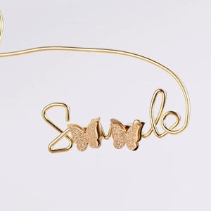 Macro detail of golden smile-shaped earrings featuring textured matte double-layer butterflies