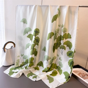 Détail d'un foulard en soie blanc avec imprimé feuilles de ginkgo vert sur un support