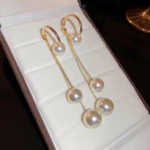 Élégantes boucles d'oreilles dorées avec trois perles graduées sur un coffret en velours