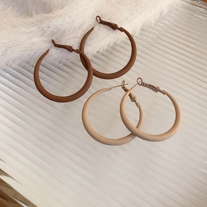 Detail of matte finish hoop earrings in dark brown and beige on a textured surface