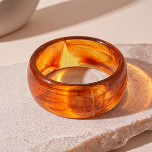 Macro shot of wide amber acrylic bangle with elegant marble texture and polished finish