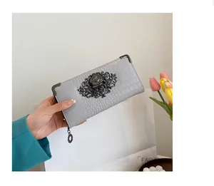 Close-up of grey long wallet with crocodile pattern and gothic skull metal ornament