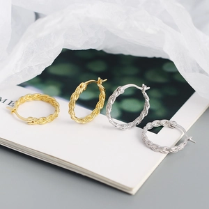 Detail of woven chain hoop earrings in gold and silver finishes on a magazine
