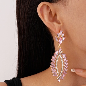 Close-up of geometric gold earrings with pink gemstones and dangling tassels on a model