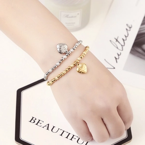 Detailed shot of gold and silver beaded bracelets with heart strawberry charms on wrist