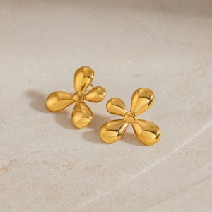 Detail of golden flower stud earrings with a polished finish on textured stone