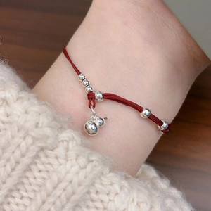 Close-up of red braided cord bracelet with silver beads and gourd pendant charm