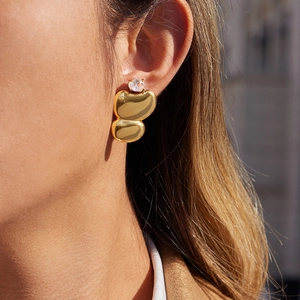 Close-up of golden asymmetric stud earrings with zircon stone on model's ear