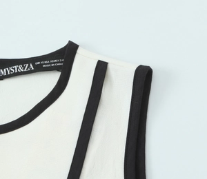 Detail of white crepe top with contrast black trim and high-quality stitching texture
