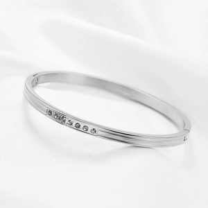 Polished silver stainless steel bangle with inlaid crystals on white silk background