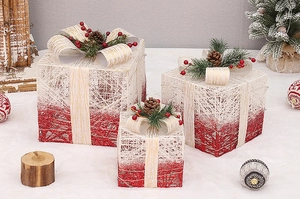 Close-up of Christmas gift box trio with red glitter, golden ribbons and pine cones