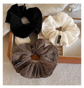 Detailed close-up of three knitted scrunchies in black, cream, and brown with woven labels