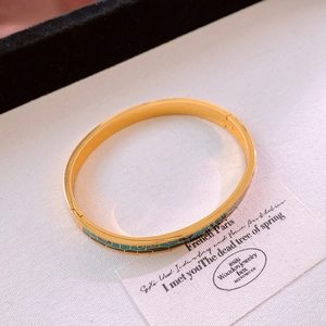 Vue détaillée macro du bracelet vintage doré avec motifs en émail vert sur un tissu beige