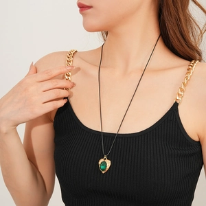 Close-up of a vintage golden heart pendant with a green gemstone on a black cord