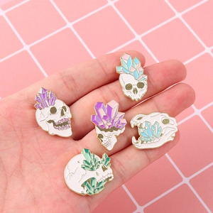 Set of gothic skull enamel pins with colorful crystals held in hand for size reference