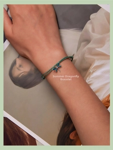 Detail of woven green cord bracelet featuring blue enamel dragonfly charm on hand