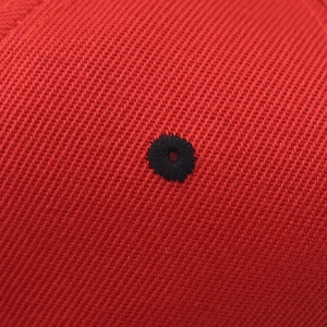 Macro detail of red twill fabric baseball cap featuring a black embroidered ventilation eyelet