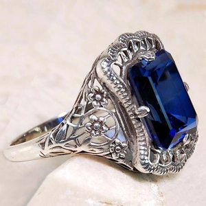 Gros plan sur une bague vintage en argent avec filigrane et pierre bleue taille émeraude