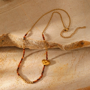 Detail of bohemian gold stainless steel necklace with brown beads and heart charm
