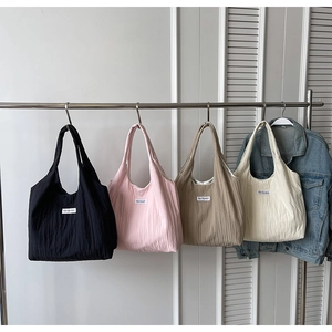 Detail von vier farbenfrohen Falten-Tote-Bags in Schwarz, Rosa und Beige an Kleiderbügeln