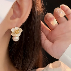 Macro detail of floral pearl earrings with white petals and diamond accents on ear lobe