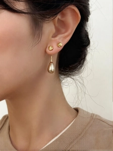 Close-up of golden teardrop pearl earring and geometric studs worn by a model