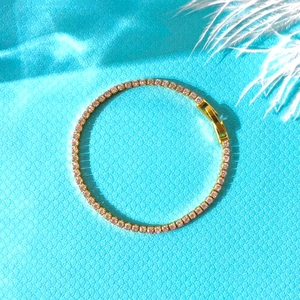 Detail of gold tennis bracelet featuring pink zircon stones on a blue fabric background