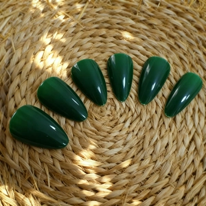 Detailed view of long almond dark green glossy press-on nails on a natural woven surface