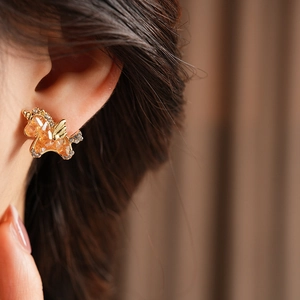 Details von goldenen Einhorn-Ohrringen mit orangefarbenen Edelsteinen am Model