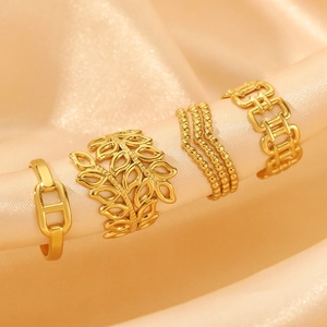 Four gold titanium steel rings set with H-shape and leaf patterns on champagne silk