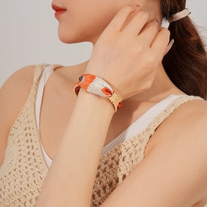 Detailed shot of an orange and beige silk scarf bracelet with golden metal accents