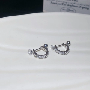 Macro shot of silver U-shaped earrings with zircons on a white ceramic tray
