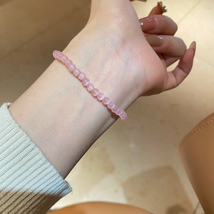 Pink cat eye stone beaded bracelet on female wrist in a warm indoor home setting