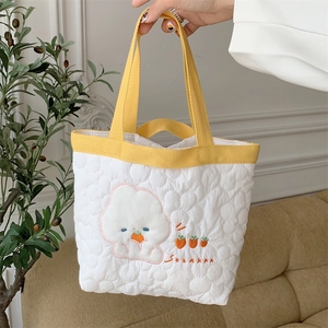 Close-up of quilted floral handbag featuring yellow handles and cute cartoon embroidery
