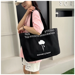 Detail of black canvas tote bag with NKK STUDIO tulip print and wide shoulder straps