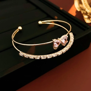 Detail of golden double-layer open bracelet with pink crystal bow and white zircon stones