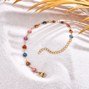 Close-up of golden heart charm bracelet with colorful glitter inlays on white beach sand