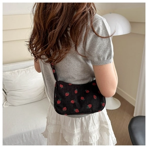 Detailed texture of black corduroy shoulder bag featuring embroidered red strawberry patterns