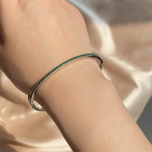 Close-up of silver bangle with micro-set green zircons on wrist with silk background