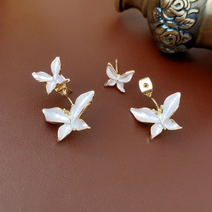Détail macro des boucles d'oreilles papillon dorées avec émail blanc nacré
