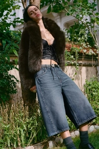 Détail d'un manteau en fausse fourrure marron avec corsage en cuir noir et short en jean