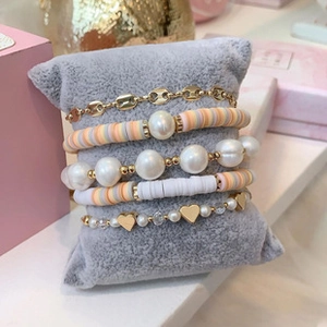 Detailed set of 5 colorful daisy and pearl beaded bracelets on a soft velvet display cushion
