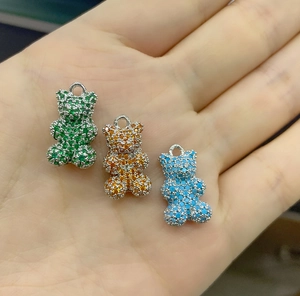 Primo piano di ciondoli a forma di orso in zirconia verde, arancio e blu in mano