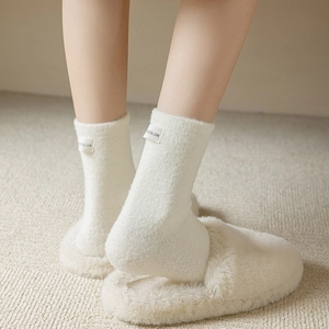 Close-up of white fluffy wool socks with a small textile brand label on a beige carpet