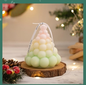 Detailed view of a gradient Christmas tree candle with a ribbon on a wooden base