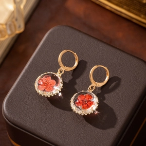 Close-up of gold drop earrings featuring red dried flowers inside clear glass spheres