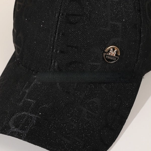 Close-up of black baseball cap with sparkling fabric texture and rhinestone M metal logo