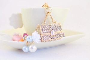 Detail of camellia keychain with rhinestones and blue pearls on a golden handbag charm