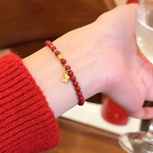 Nahaufnahme eines Armbands aus roten Achatperlen mit goldenem Schmetterling am Handgelenk