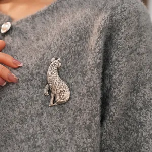 Vintage antique silver cat brooch with textured metal engraving on a grey sweater